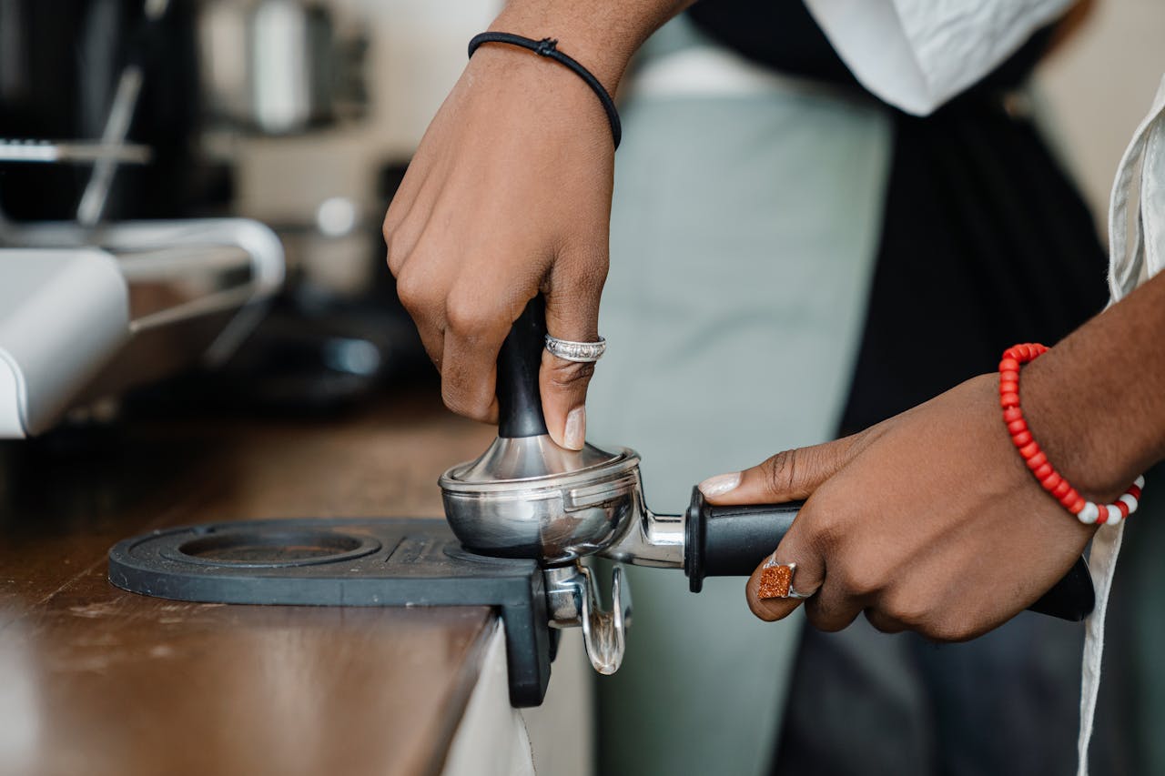 Close-up of a barista using a tamper to prepare espresso in a coffee shop.